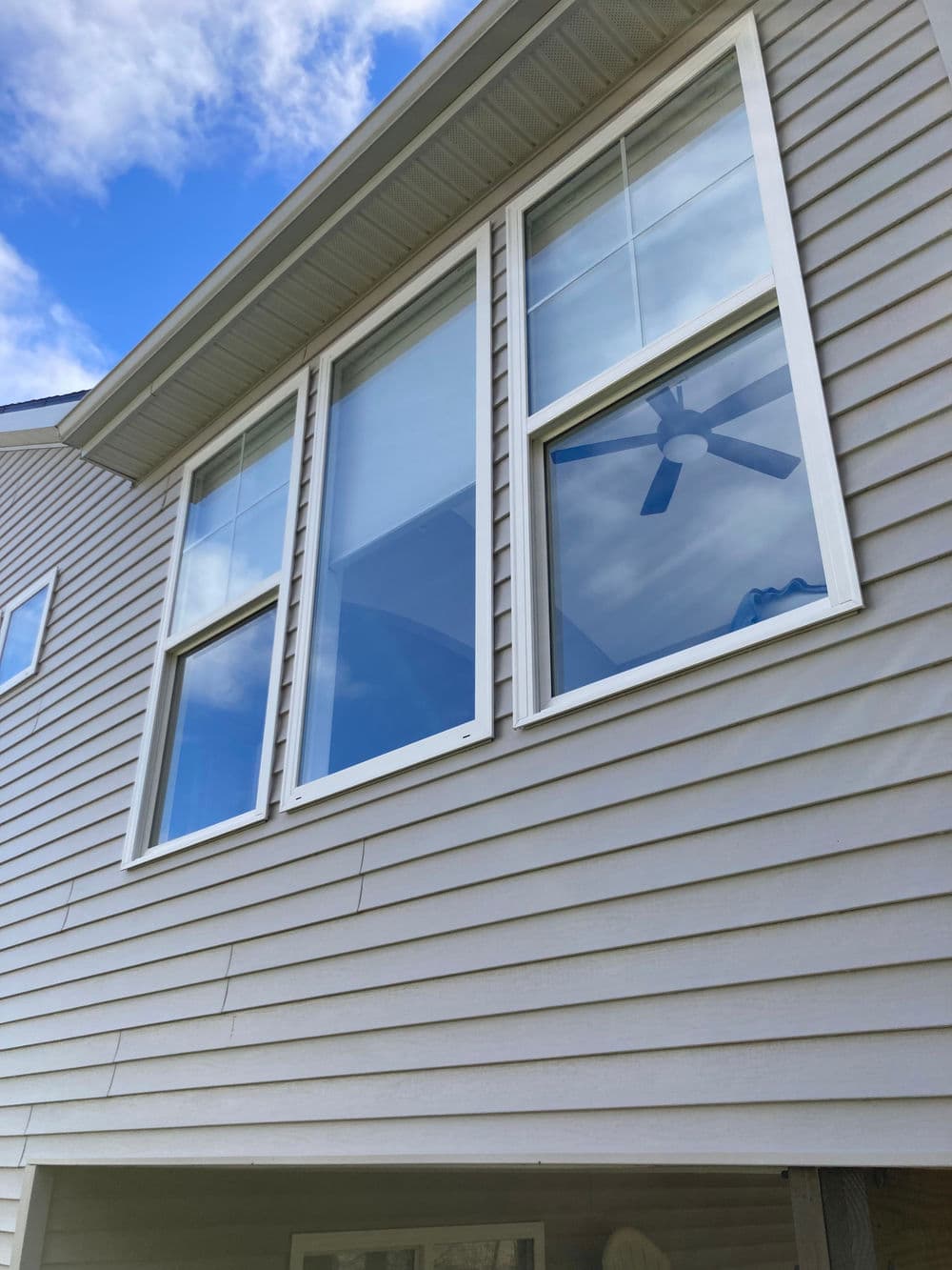 Modern house exterior featuring large windows and a ceiling fan against a blue sky.
