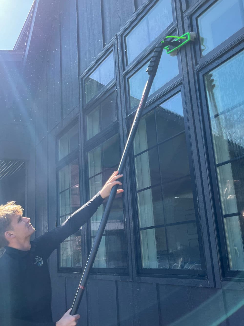 Person using a pole to clean large windows on a black modern building exterior.