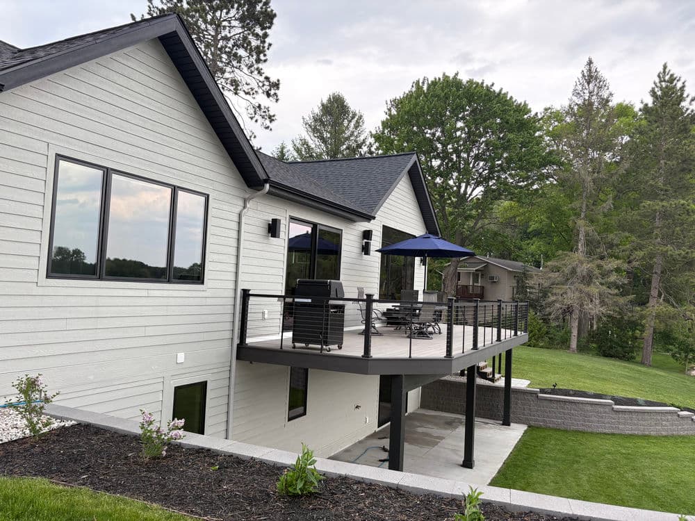 Modern home exterior with a large deck, stylish furniture, and lush greenery in the background.