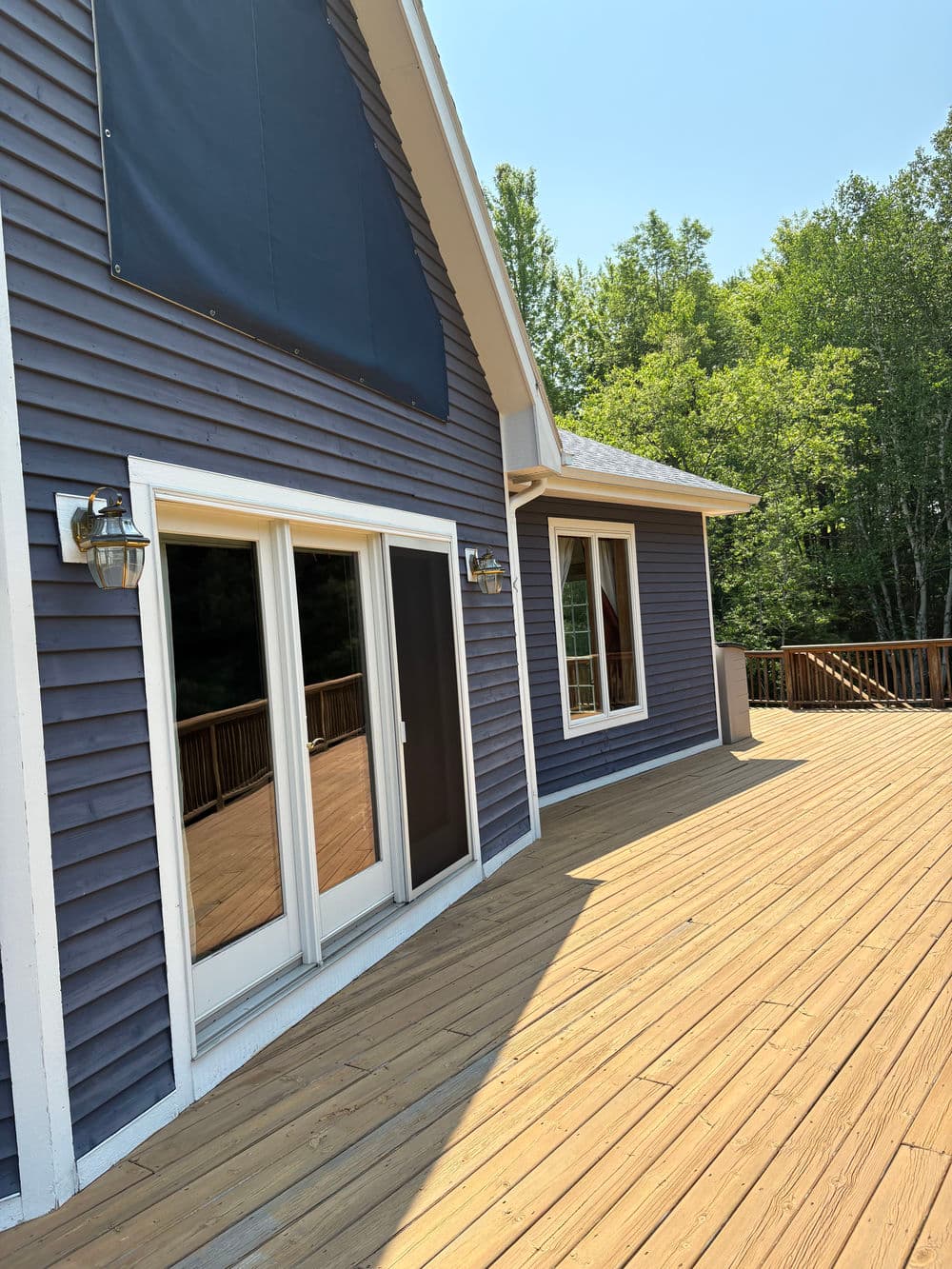 Modern home exterior showcasing a spacious wooden deck and large glass doors. Lush greenery in background.