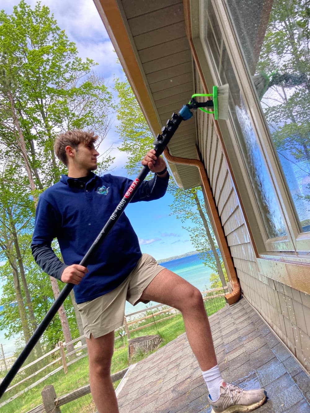 Teen window washing with a pole squeegee near a lake and trees, showcasing summer outdoor cleaning.