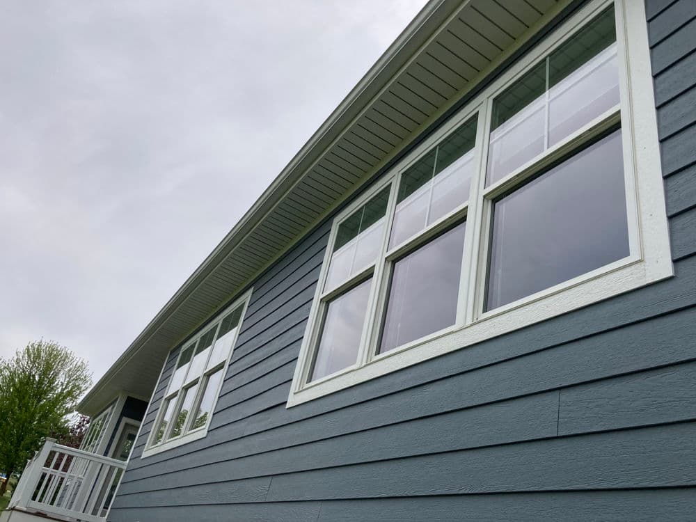 Modern gray house exterior with large windows and white trim against cloudy sky.