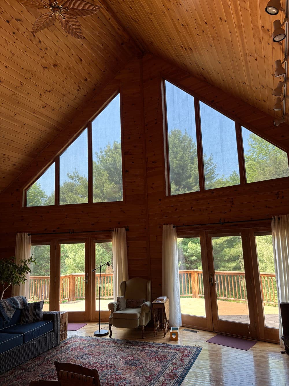 Bright wooden cabin interior with large triangular windows and a cozy seating area.