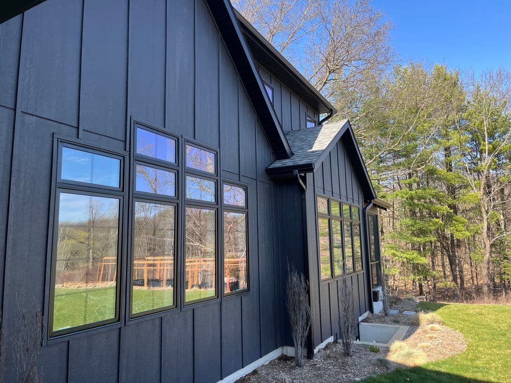 Modern black house exterior with large windows and serene natural surroundings.