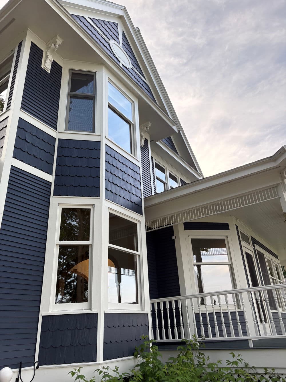 Victorian-style blue house with intricate shingles and large windows against a cloudy sky.