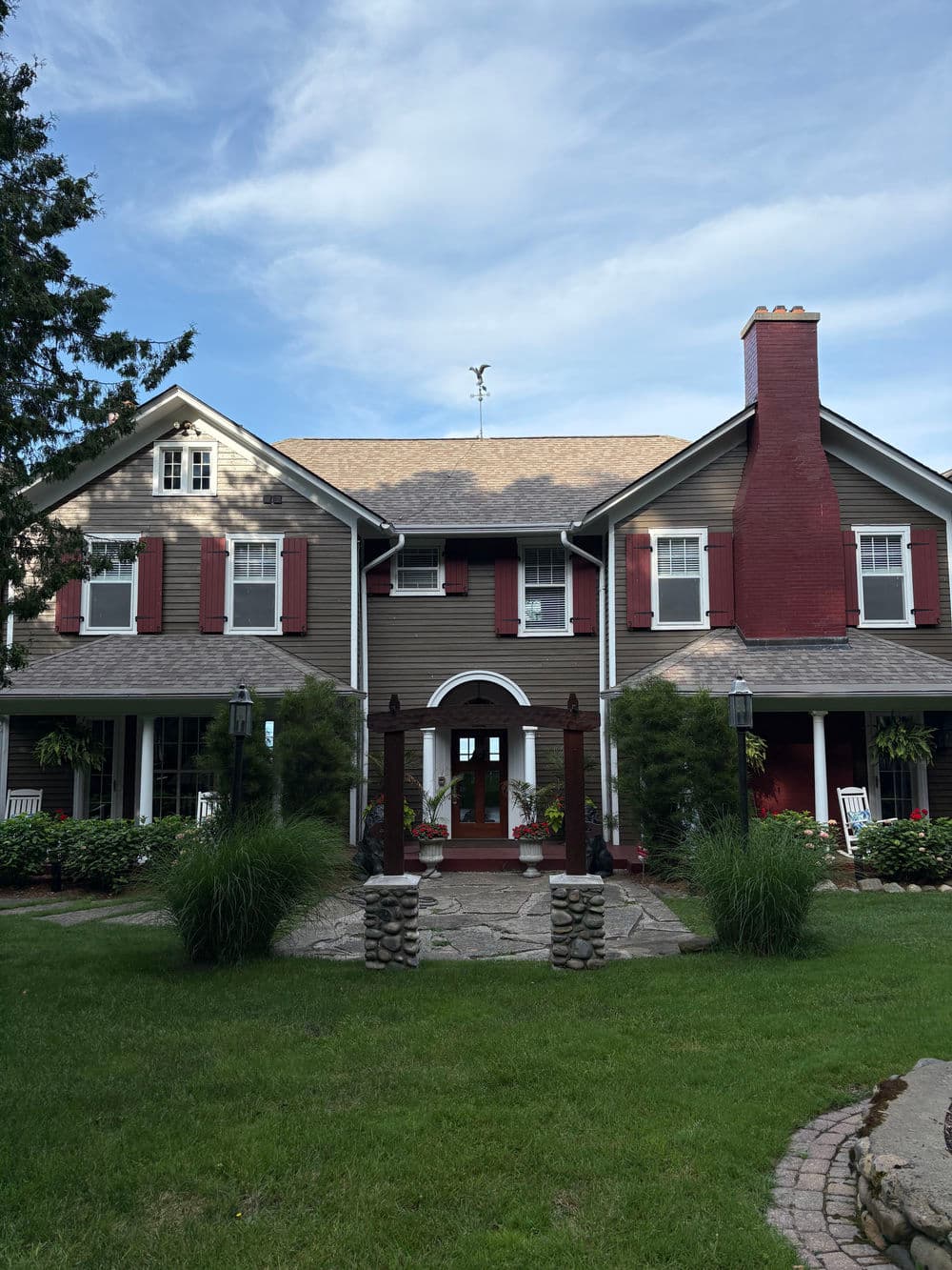 Charming two-story house with red shutters, porch, and landscaped lawn under blue sky.
